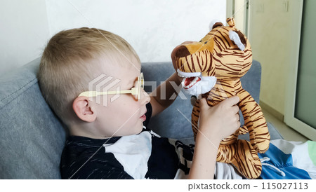 A boy brushes his teeth with a toy with an artificial jaw. Playing as a dentist, professional preparation of a child for the profession of a pediatric dentist. Hygiene and dental care A boy brushes his teeth with a toy with an artificial jaw. Playing as a dentist, professional preparation of a child for the profession of a pediatric dentist. Hygiene and dental care 115027113