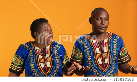 Unsure african american people doing i dont know sign in studio, showing doubtful clueless gesture on camera. Man and woman being uncertain, posing over orange background. Unsure african american people doing i dont know sign in studio, showing doubtful clueless gesture on camera. Man and woman being uncertain, posing over orange background. 115027168
