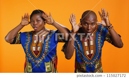 African american silly couple fooling around on camera, sticking tongue out and having fun with jokes in studio. Ethnic man and woman laughing together and acting playful. African american silly couple fooling around on camera, sticking tongue out and having fun with jokes in studio. Ethnic man and woman laughing together and acting playful. 115027172