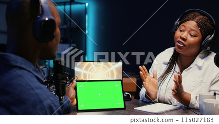 Woman invited to podcast watching internet clips on green screen tablet with host in studio, discussing content. African american guest reacting to videos on mockup device during online comedy show Woman invited to podcast watching internet clips on green screen tablet with host in studio, discussing content. African american guest reacting to videos on mockup device during online comedy show 115027183