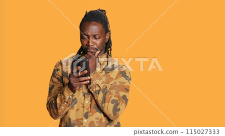 Modern guy navigating online websites on smartphone, checking his chats for texts and posing on camera. African american person using mobile apps to stay connected with friends. Handheld shot. Modern guy navigating online websites on smartphone, checking his chats for texts and posing on camera. African american person using mobile apps to stay connected with friends. Handheld shot. 115027333