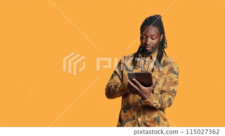 Modern person navigating online on tablet in studio, using mobile device to check social media apps and browse internet pages. African american man checking websites on gadget. Modern person navigating online on tablet in studio, using mobile device to check social media apps and browse internet pages. African american man checking websites on gadget. 115027362