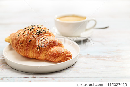 Freshly baked Croissant and a cup of Coffee artfully presented on a White Wooden Table Freshly baked Croissant and a cup of Coffee artfully presented on a White Wooden Table 115027413