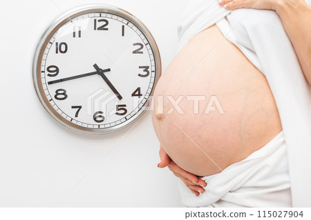 Pregnant Woman Holding Belly Next to Wall Clock Pregnant Woman Holding Belly Next to Wall Clock 115027904