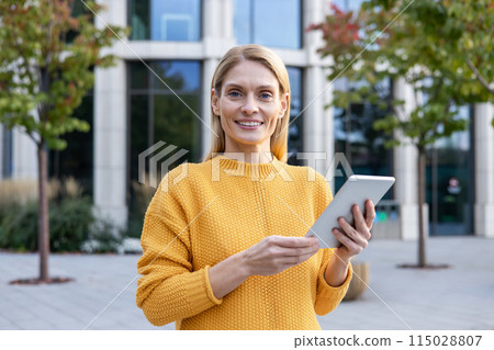 Confident professional woman in a yellow sweater using a tablet outside a modern office building. Represents technology in everyday business. Confident professional woman in a yellow sweater using a tablet outside a modern office building. Represents technology in everyday business. 115028807