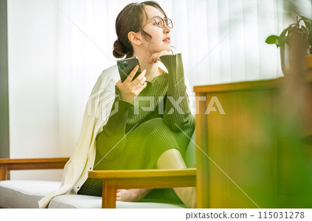 Woman sitting on sofa at home looking out the window 115031278