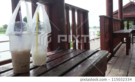 Plastic coffee cup and milk cup place on a red wooden bench in afternoon sunlight 115032334