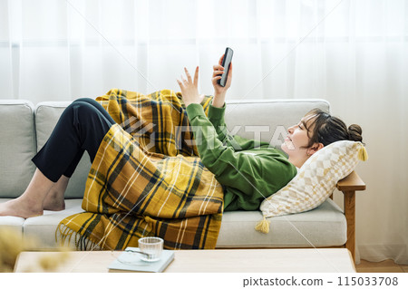 Woman looking at smartphone on sofa at home 115033708