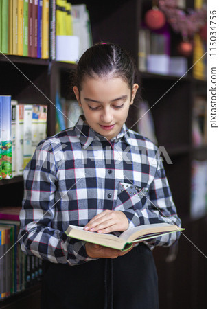 Beautiful schoolgirl reading a book in the library 115034756