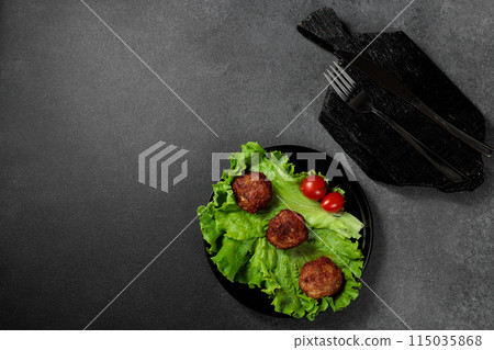 Fried cutlets on a lettuce leaf with tomato on a black background 115035868