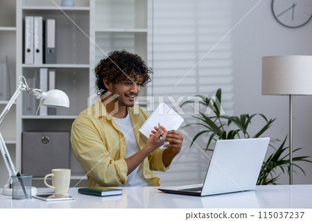 Smiling man working from home, holding a notebook and engaging in a virtual meeting from his home office. Remote work concept. Smiling man working from home, holding a notebook and engaging in a virtual meeting from his home office. Remote work concept. 115037237