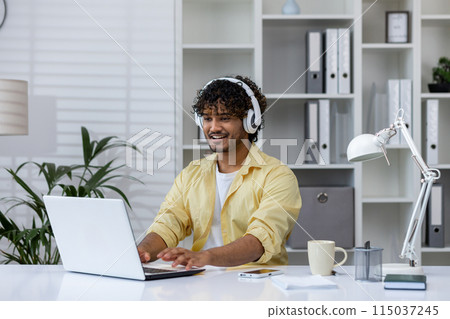 Man wearing headphones and working on a laptop in a comfortable, well-organized home office setting, emphasizing remote work and technology. Man wearing headphones and working on a laptop in a comfortable, well-organized home office setting, emphasizing remote work and technology. 115037245