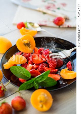 fresh fruit salad of ripe strawberries and apricots, on a light wooden table 115037348