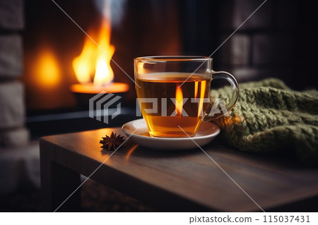 A cup of tea sits on a table next to a crackling fireplace 115037431