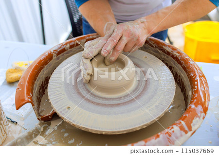 Worker creating bowl with wet soft clay using potter wheel 115037669