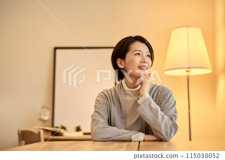 A woman with a relaxed expression in a room with warm indoor lighting 115038052