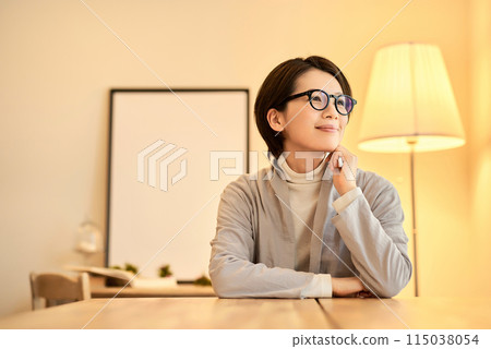 A woman with a relaxed expression in a room with warm indoor lighting 115038054