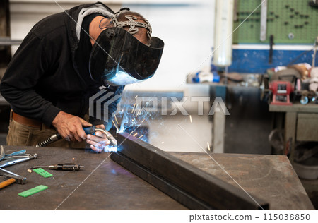 Spectacular conceptual image of a blacksmith busy using the welding machine. Sparks and smoke flash from the tip of the soldering iron. Blurred background. Welding, repair, work concept. Copy space. 115038850