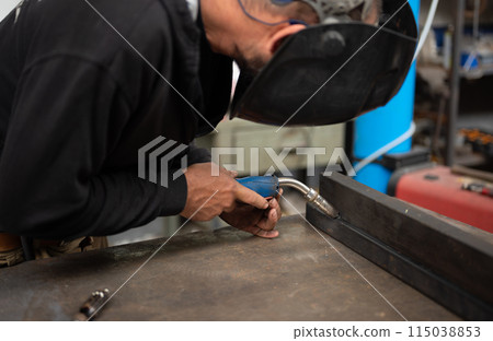 Conceptual image of a blacksmith busy using the welding machine. Place the tip of the soldering iron on the point to be fixed. Blurred workshop background. Welding, repair, work concept. Copy space. Conceptual image of a blacksmith busy using the welding machine. Place the tip of the soldering iron on the point to be fixed. Blurred workshop background. Welding, repair, work concept. Copy space. 115038853