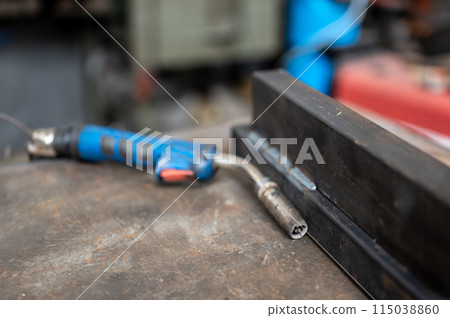 Close-up on the welding gun, next to two welded metal bars. Conceptual image of work, metalworking, craftsmanship. Copy space. 115038860
