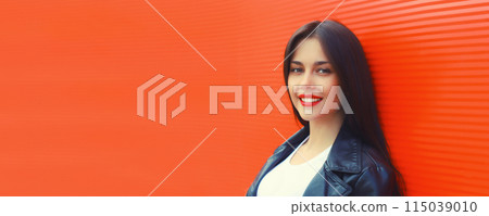 Portrait of beautiful brunette smiling young woman model posing in black leather jacket on red 115039010