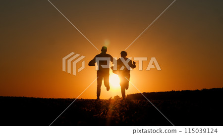 Against the backdrop of the setting sun, two businessmen's silhouettes dance merrily, with a tablet in one man's hand. Against the backdrop of the setting sun, two businessmen's silhouettes dance merrily, with a tablet in one man's hand. 115039124