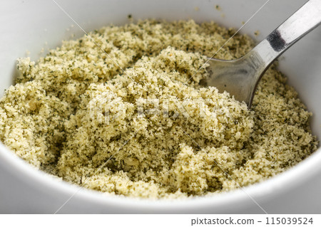 Ground crushed pumpkin seeds as a raw ingredient for dietary pastry in white kitchen cup with spoon 115039524