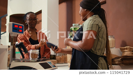 Woman using card payment at pos to buy fresh produce, choosing ripe colorful fruits and vegetables for healthy nutrition. Client paying for organic locally grown goods at checkout. Handheld shot. Woman using card payment at pos to buy fresh produce, choosing ripe colorful fruits and vegetables for healthy nutrition. Client paying for organic locally grown goods at checkout. Handheld shot. 115041729