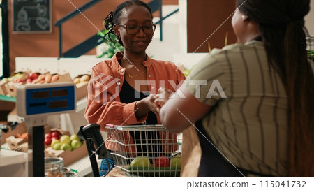 Regular client purchasing multiple bulk items at local market, choosing fruits and veggies freshly harvested. Small business owner serving woman with eco friendly organic produce, healthy eating. Regular client purchasing multiple bulk items at local market, choosing fruits and veggies freshly harvested. Small business owner serving woman with eco friendly organic produce, healthy eating. 115041732