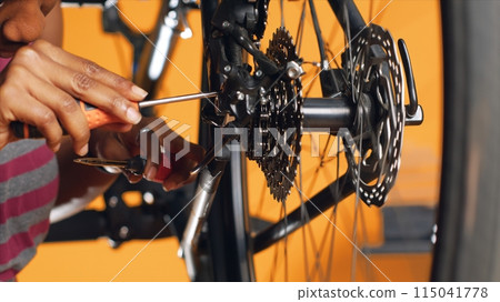 Technician pushing pedals to rotate bike wheel, inspecting it, using screwdriver and hex socket wrench to fix it, close up shot. Professional testing bike crank arm and chain rings, studio background 115041778