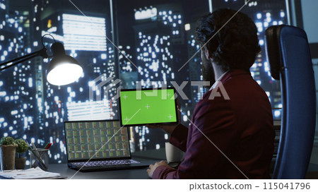 Private equity associate uses greenscreen display on tablet, sitting at workstation inside skyscraper. Influential chairman looks at gadget with blank copyspace template screen, legal work. 115041796