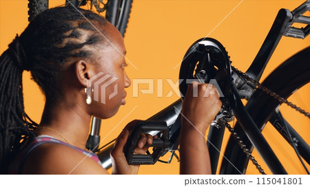 African american woman pushing pedals to spin bike wheel, inspecting it, using screwdriver and hex socket wrench to fix it, close up shot. Riding hobbyist testing bicycle crank arm and chain rings 115041801
