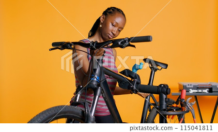 BIPOC mechanic setting up bike repair stand, using it to adjust handlebar and fix broken wheels, studio background. Professional placing bicycle on workstand in tight grip to inspect it, camera B BIPOC mechanic setting up bike repair stand, using it to adjust handlebar and fix broken wheels, studio background. Professional placing bicycle on workstand in tight grip to inspect it, camera B 115041811