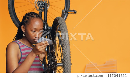 African american woman using specialized glue to repair broken bicycle chain, studio background. Skilled engineer applying adhesive on bike components during maintenance process, camera A African american woman using specialized glue to repair broken bicycle chain, studio background. Skilled engineer applying adhesive on bike components during maintenance process, camera A 115041831