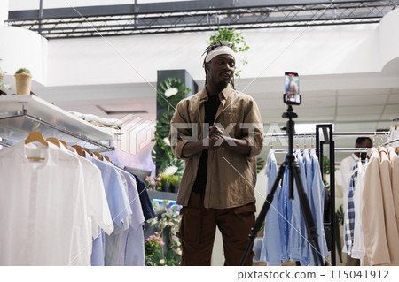 African american blogger recording promotional video in clothing store to attract customers. Stylist talking about new fashion collection on smartphone camera and advertising brand in shop 115041912
