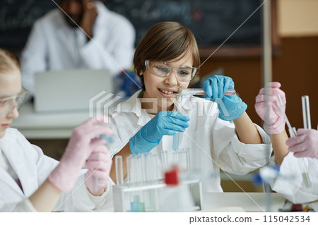 Curious Caucasian boy sitting at table in classroom mixing liquids in test tube during lab experiment in Chemistry class 115042534