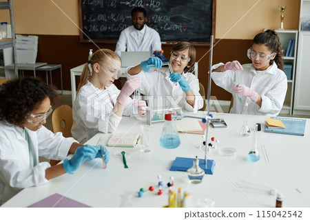 Multi-ethnic group of kids doing lab experiment in classroom during Chemistry lesson at school, high angle view shot 115042542