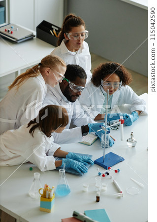 Vertical high angle view of young African American teacher and group of middle school students doing experiments during Chemistry class Vertical high angle view of young African American teacher and group of middle school students doing experiments during Chemistry class 115042590