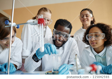 Cheerful African American teacher and group of ethnically diverse kids doing lab experiment during Chemistry class 115042593