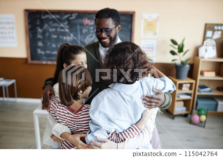 Cheerful African American teacher and multi-ethnic group of kids standing in classroom and hugging, copy space 115042764