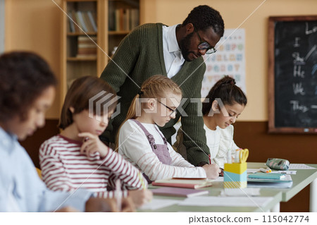 African American male teacher of English working in class watching kids doing writing exercise 115042774