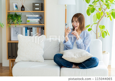 Young woman looking at her smartphone in the living room 115044065