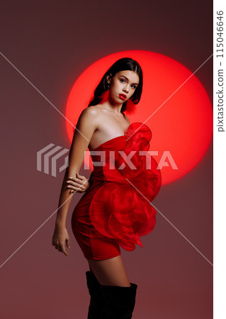 A young girl in a red dress posing in the studio against the backdrop of a red spotlight. A young girl in a red dress posing in the studio against the backdrop of a red spotlight. 115046646
