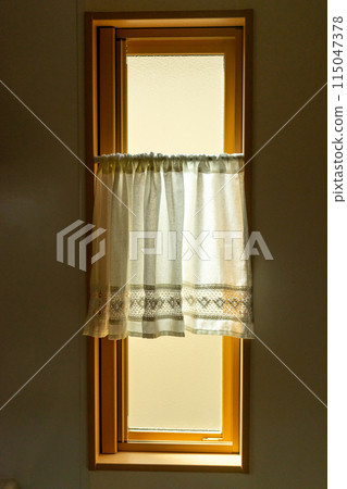 A kitchen window with a frosted glass vertical sliding window and cafe curtains 115047378
