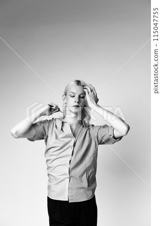 Black and white photo of man with make up on one half of his face. Man wearing fashionable shirt divided on two colours. Man isolated on grey background. Black and white photo of man with make up on one half of his face. Man wearing fashionable shirt divided on two colours. Man isolated on grey background. 115047755