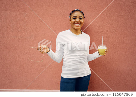 Young black woman with afro hairstyle smiling in a city. Mixed girl with cocktail. Young black woman with afro hairstyle smiling in a city. Mixed girl with cocktail. 115047809