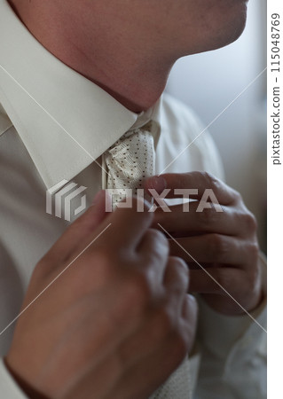 A man adjusts his tie before a formal event, ensuring a sharp and elegant appearance 115048769