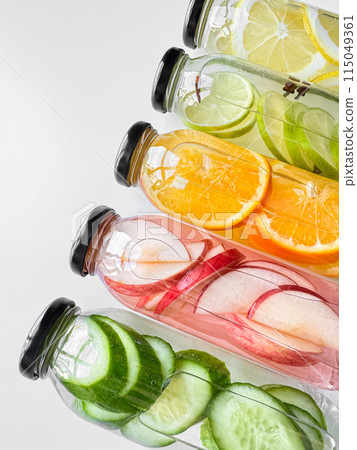Stacked glass bottles with detox drinks with cucumber, apple, orange, and lemon slices on white background. Vertical orientation, refreshing beverage concept for design and print. Stacked glass bottles with detox drinks with cucumber, apple, orange, and lemon slices on white background. Vertical orientation, refreshing beverage concept for design and print. 115049361