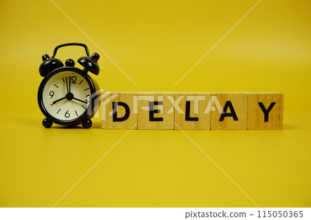 Delay with wooden blocks alphabet letters and alarm clock on yellow background Delay with wooden blocks alphabet letters and alarm clock on yellow background 115050365