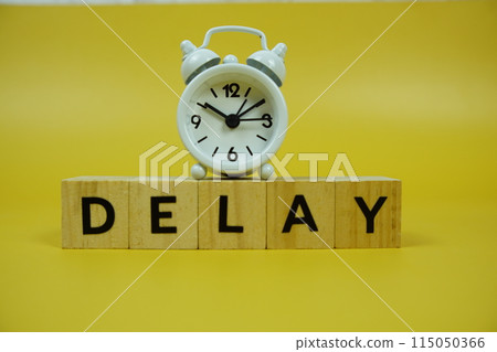 Delay with wooden blocks alphabet letters and alarm clock on yellow background Delay with wooden blocks alphabet letters and alarm clock on yellow background 115050366